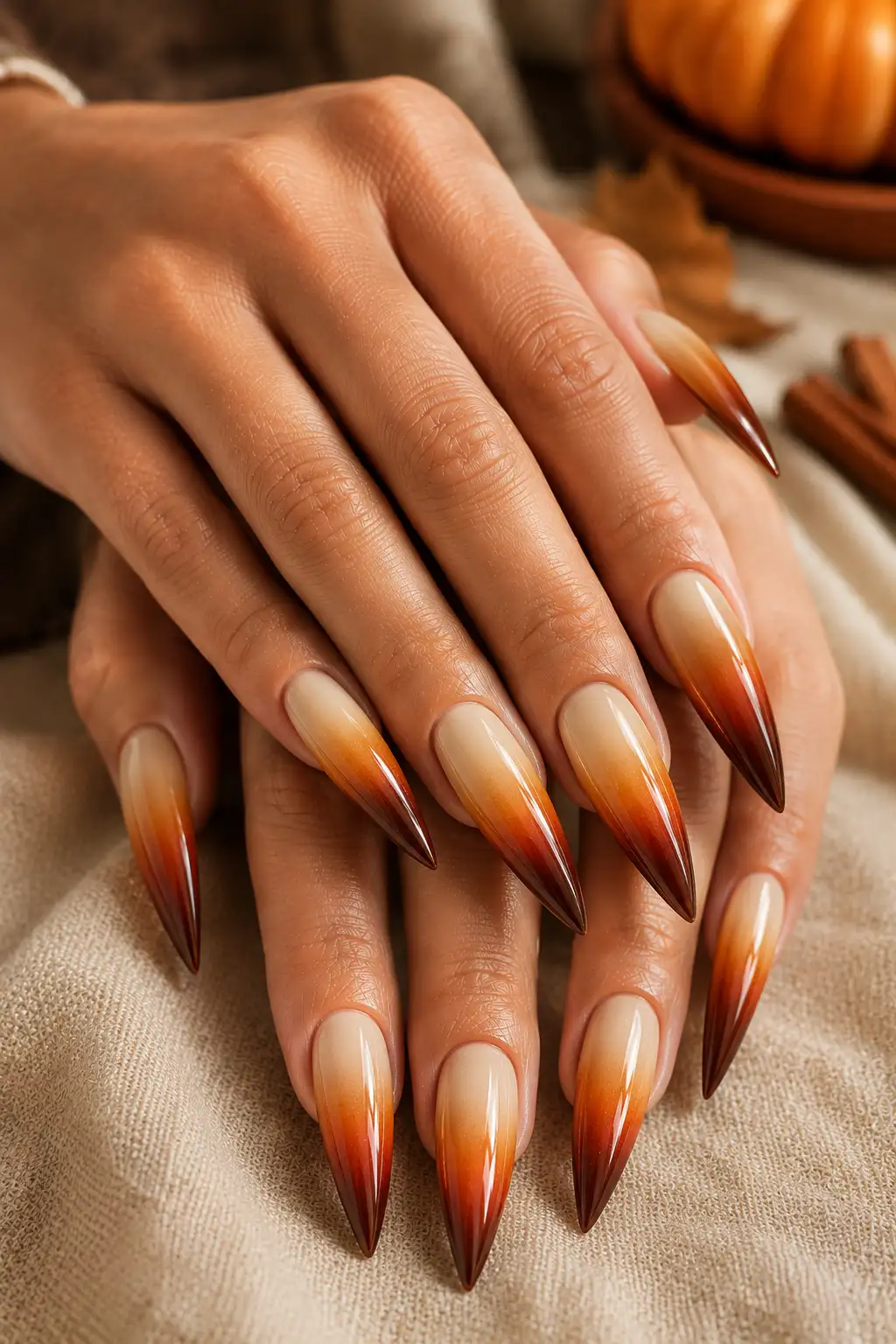 Long pointed stiletto nails featuring a glossy multi-tone gradient transitioning from creamy ivory through caramel and pumpkin orange to deep cinnamon.