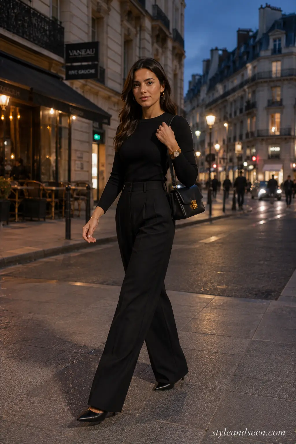 Young woman wearing an all-black outfit with wide-leg trousers, a structured handbag, and gold accessories for a stylish night-out look.