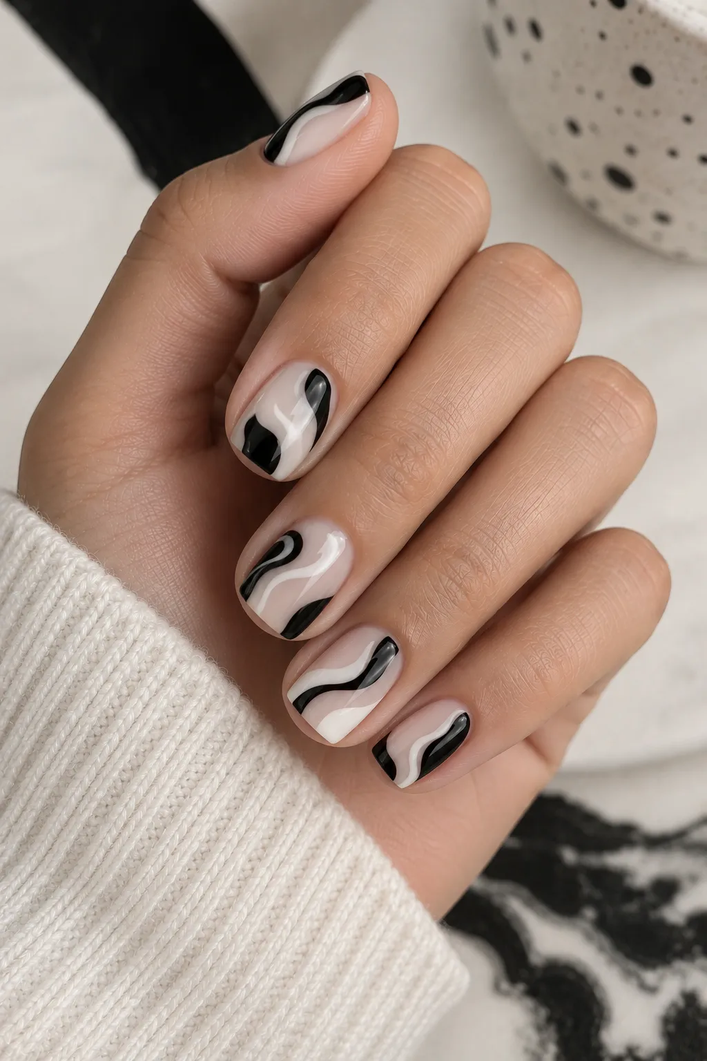 Short square nails with a milky base decorated with elegant glossy black abstract swirl details in a modern nail-art design.
