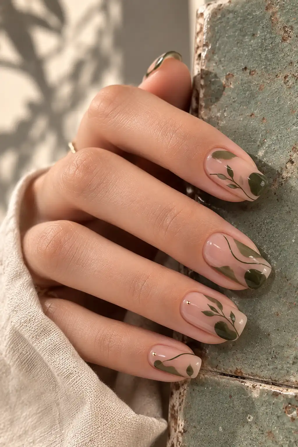 Transparent nude squoval nails decorated with abstract moss-green stems, delicate leaves, botanical shapes, and tiny gold accents.