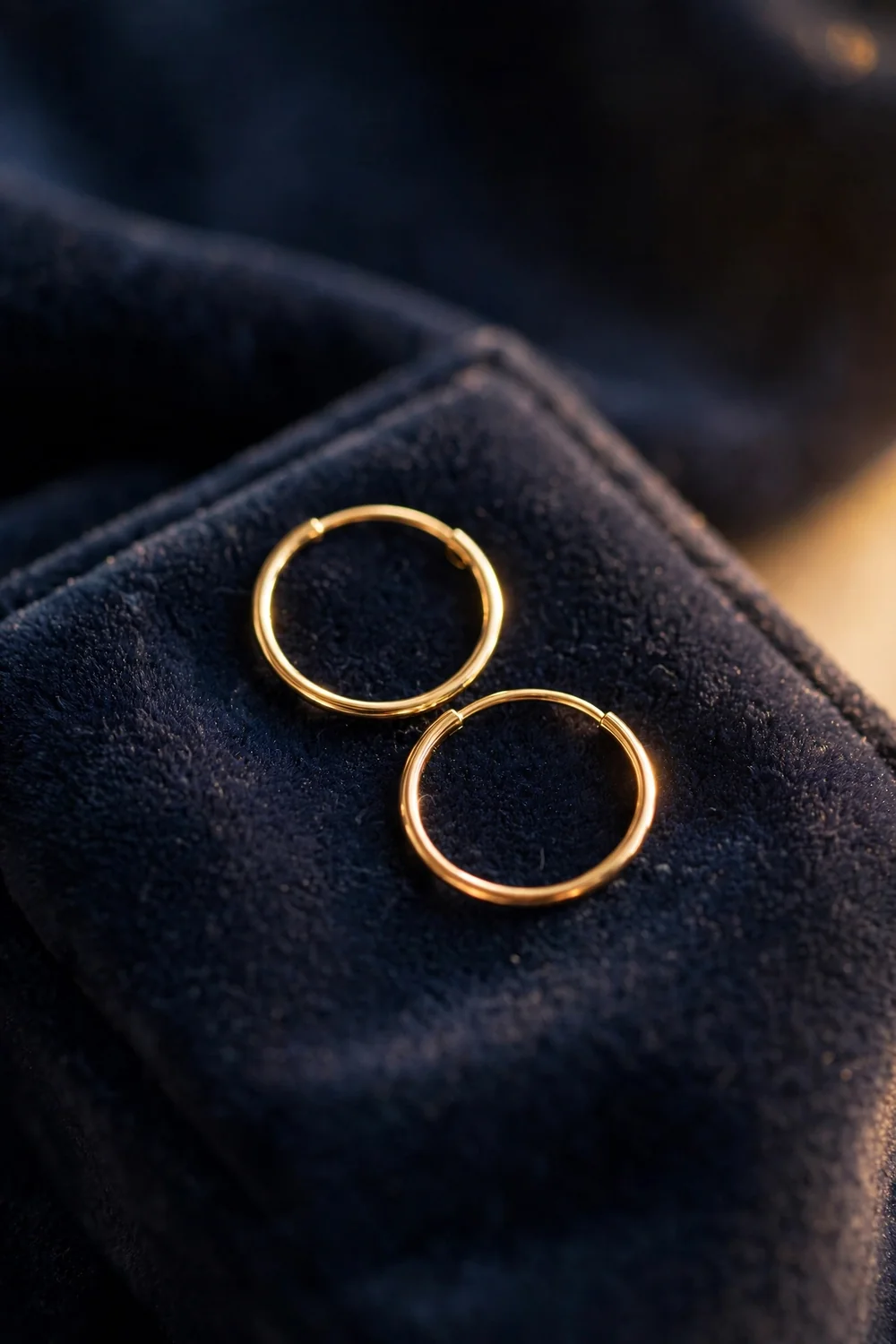 Dainty gold hoop earrings on a velvet pad in warm light