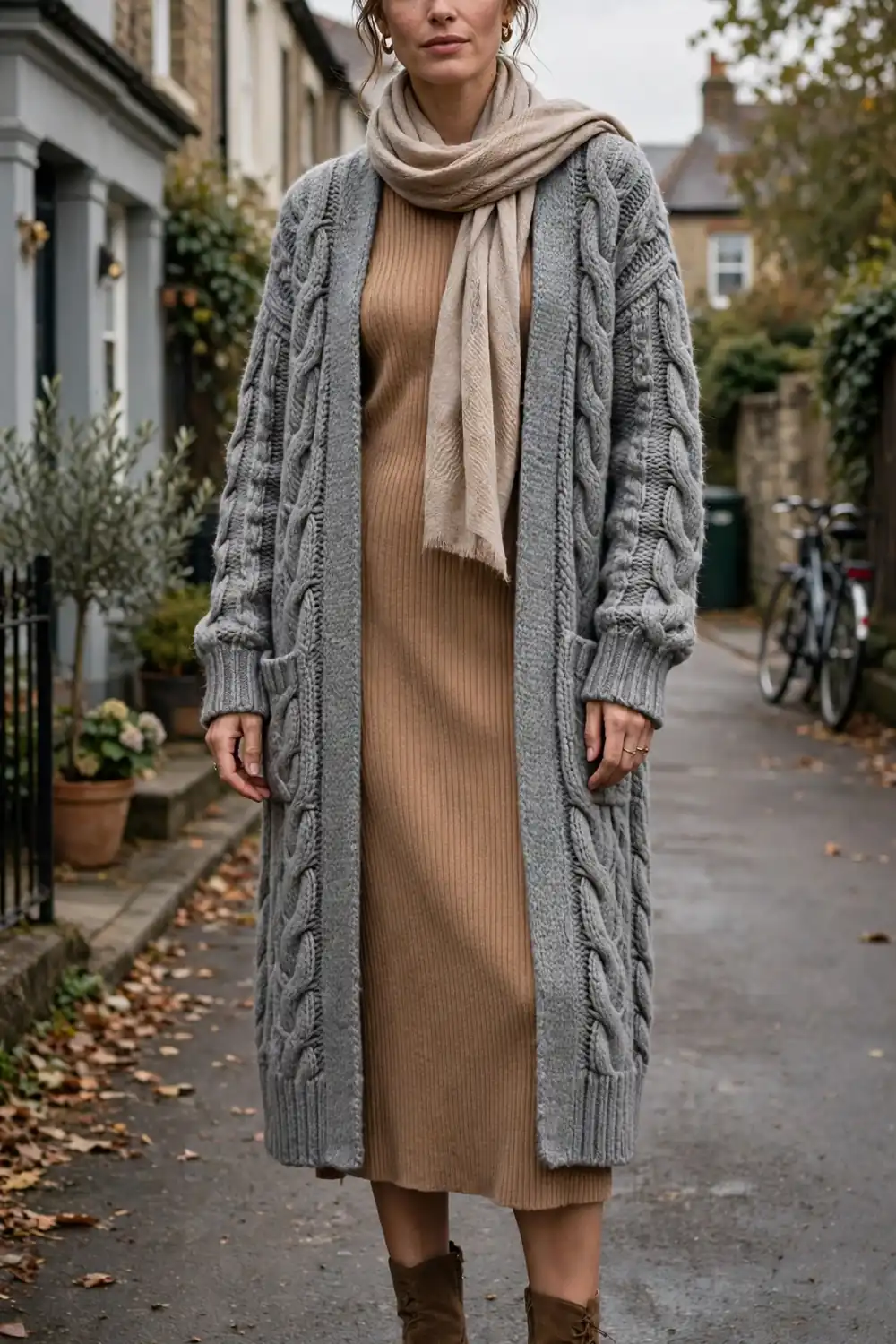 Woman in a camel sweater dress layered under a long grey knit cardigan with ankle boots