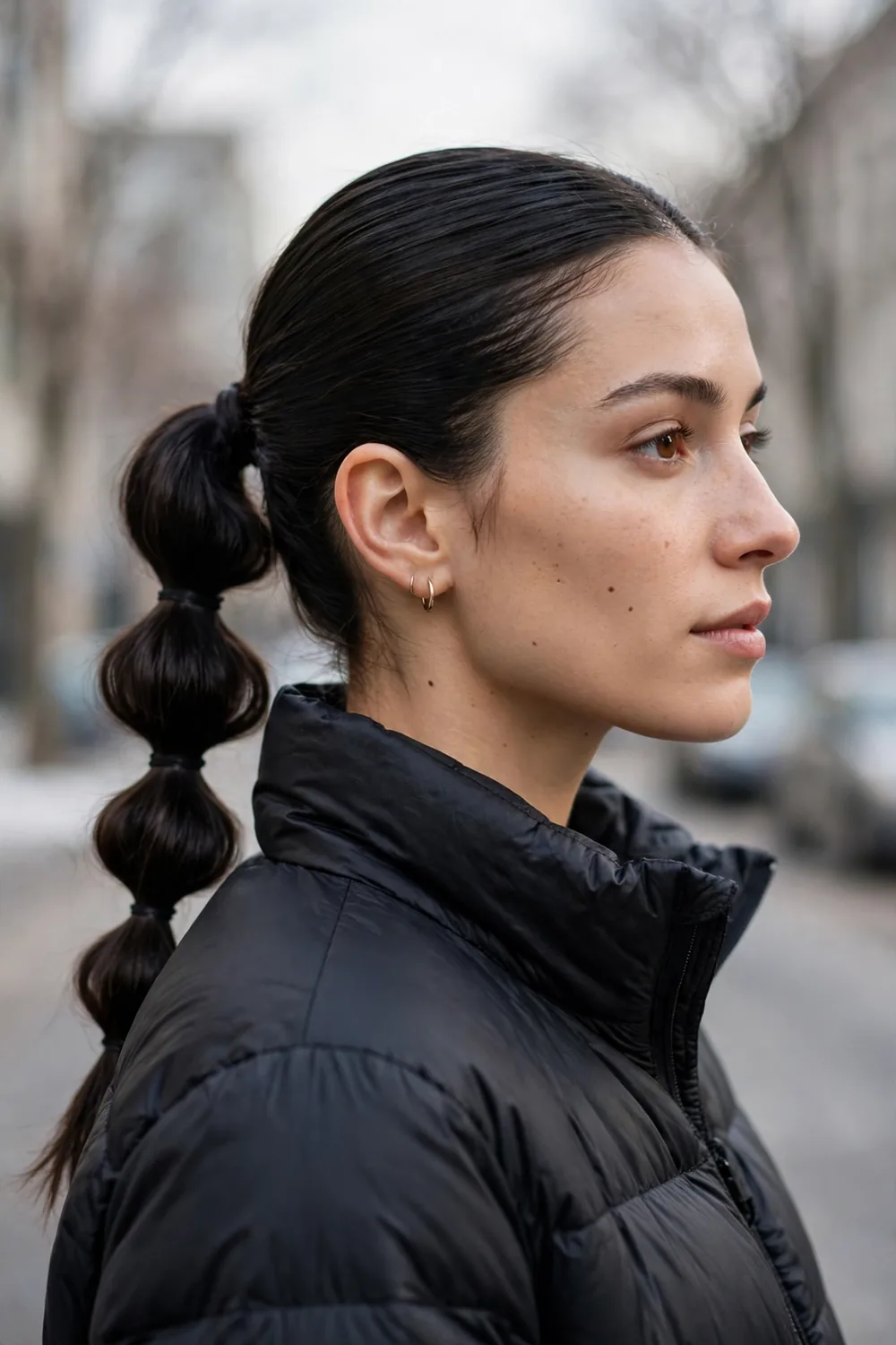 Low bubble ponytail with soft rounded sections tied with clear elastics on sleek hair