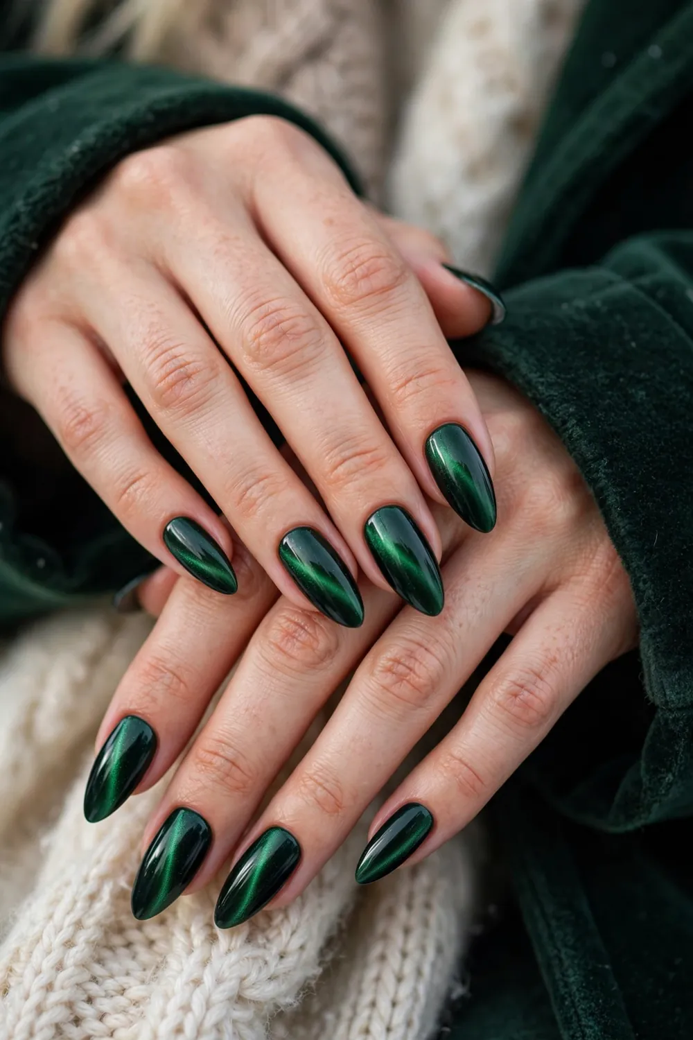 Close up of hands with emerald green velvet cat eye nails in luxurious winter styling