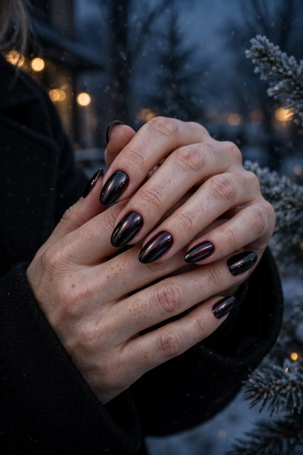 Close up of hands with black cherry chrome nails in a moody winter evening look